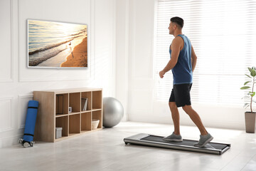 Canvas Print - Sporty man training on walking treadmill and watching TV at home