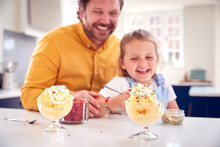 Father And Daughter In Kitchen Decorating Ice Cream Dessert With Cream And Sprinkles