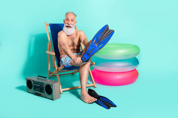 Wall Mural - Photo of pretty cute retired man naked torso sitting beach chair wearing flippers listening boombox isolated turquoise color background