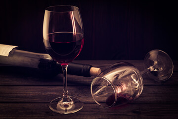 Bottle of red wine with two glasses on an old wooden table. Focus on an overturned glass of wine