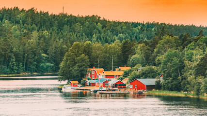 Poster - Sweden. Many Beautiful Red Swedish Wooden Log Cabins Houses On Rocky Island Coast In Summer Evening. Lake Or River Landscape