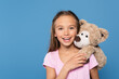 © LIGHTFIELD STUDIOS - Kid with soft toy smiling at camera isolated on blue