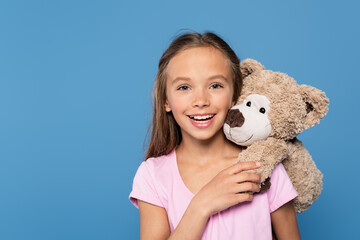 Wall Mural - Kid with soft toy smiling at camera isolated on blue