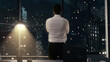 © Iokanan Pro - Back view of thoughtful Businessman standing in his office working late at night, looking out of the window as it rains contemplating his next big idea.