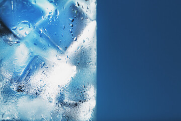 Glass with water and ice cubes on a blue background