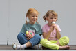Two little Caucasian cute girls are sitting cross-legged and eating ice cream.