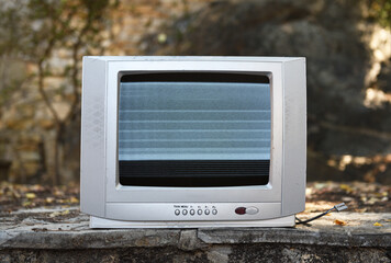 An old silver TV with noise on the screen stands in the woods. Vintage TVs 1980s 1990s 2000s. 