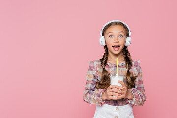 Wall Mural - Excited kid in headphones holding milkshake isolated on pink