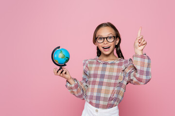 Wall Mural - amazed girl with small globe showing idea gesture while looking at camera isolated on pink