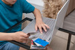 © Anna - Boy is sitting near laptop with credit card in hands and making online payment. Internet shopping from home.