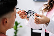 Doctora colocando gafas de pruebas en el rostro de un joven mientras le hacen el examen de la vista 