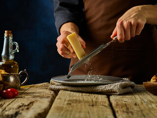 Wall Mural - A professional chef grates Parmesan cheese. Caesar salad preparation process. Rough wooden table. Country style. Home kitchen. Restaurant dish. Lots of ingredients. Close-up. Careful viewing.