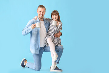 Wall Mural - Happy daughter and father with cups of hot cocoa on color background