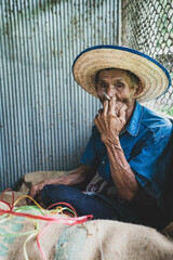 Canvas Print - Close up of  An old Southeast Asian man is smoking and sewing sacks at the rice mill factory.