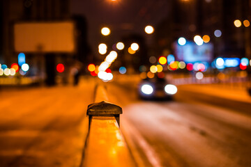 Wall Mural - Winter night in the big city, pavement with billboard and the headlights of the approaching car on the road. Close up view from the handrail on the sidewalk level