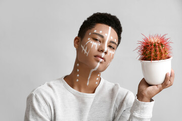 Poster - Young African-American guy with paint on face and cactus against light background