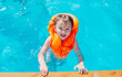 © Яна Айбазова - a little girl in an orange life jacket swims in the pool and looks at the camera