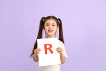 Little Girl Holding Paper Sheet With Letter R On Color Background