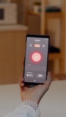 Female holding smartphone with lighting control application, turning on the lights sitting in kitchen house with automation lighting system. Woman using high technology software, wireless switch on