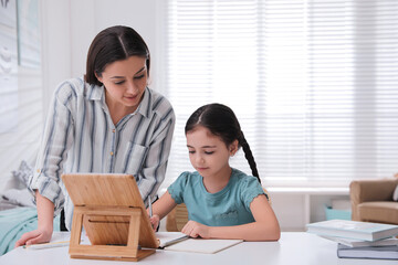 Wall Mural - Mother helping her daughter doing homework with tablet at home