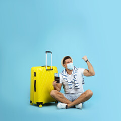 Poster - Male tourist in protective mask holding passport with ticket and suitcase on turquoise background, space for text