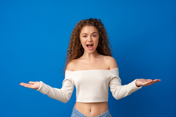 amazed young woman holding two blank spaces for advertising on blue background