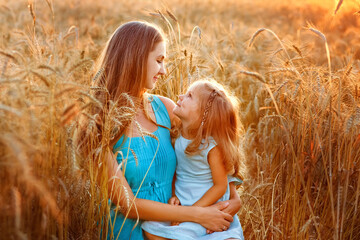 Mother and daughter embrace in a wheat field at sunset. They sit among the ears and look at each other. Agro walk in the countryside