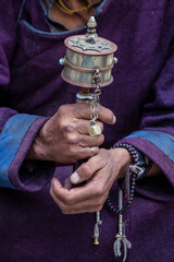 Wall Mural - Old Tibetan woman holding buddhist prayer wheel in Hemis monastery, Ladakh, India. Hand and prayer wheel, close up