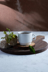 Canvas Print - Vertical shot of a cup of coffee on a wooden board with rocks and a twig