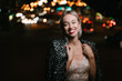 Beautiful blonde woman smiling looking at camera outdoors at night city lights street. Stylish fancy Glided dress and jacket. Happy summer evenings. Night life. Wide teeth smile red lips. Bokeh 