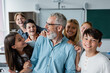 © LIGHTFIELD STUDIOS - happy multiethnic pupils embracing laughing teacher in classroom