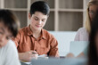 © LIGHTFIELD STUDIOS - Schoolboy holding pen near notebook and blurred multiethnic pupils