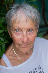 Mature woman looking at camera. Senior lady smiling in her garden. Close-up happy female face. Portrait of female model posing on camera outdoors. Elderly woman with positive emotions