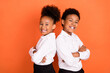 © deagreez - Profile side photo of two young black kids happy positive smile pupil uniform crossed hands isolated over orange color background