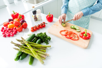 Wall Mural - Cropped top view woman in apron cutting cucumber for salad in the kitchen