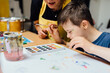 © Iryna - Young female teacher explain, talk at desk with a down syndrome schoolboy. Color painting for disabled kids, child who are down syndrome and student teacher, development of children with spesial needs