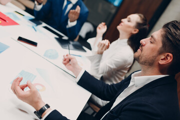 Businessman and businesswoman team meditate and holds hands each other after office meeting. Business people group conference discussion meditation concept