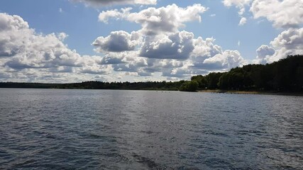 Wall Mural - Motor boat trip along the waves of the picturesque Senezh lake. Skyline, green trees on the shore and cloudy blue sky on a sunny day. Moscow region, Russia