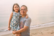 © dul_ny - Portrait middle-aged Asian father holding his daughter in his arms on the beach. Blurred background of the sea, blank space for copy and design.