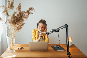 Woman podcaster streaming and broadcasting her podcast from homemade studio. Female recording podcast from home and talking into a microphone.