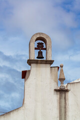 Detail of small bell tower and pinnacle on top of Portuguese Christian chapel against the cloudy blue sky