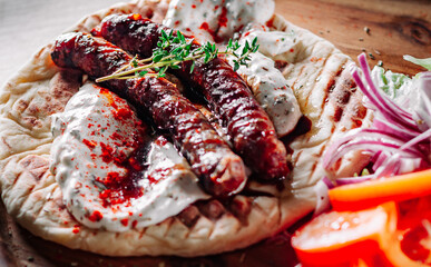 grilled meat sausages with pita bread and vegetables salad and tzatziki dip on wooden board