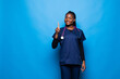 African american doctor woman in medical gown doing selfie shot on mobile phone point finger up with new idea isolated on blue background. Health care personnel medicine concept. Mock up copy space