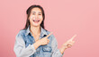 © sorapop - Asian happy portrait beautiful cute young woman wear denim standing pointing finger side away presenting product looking to camera, studio shot isolated on pink background with copy space