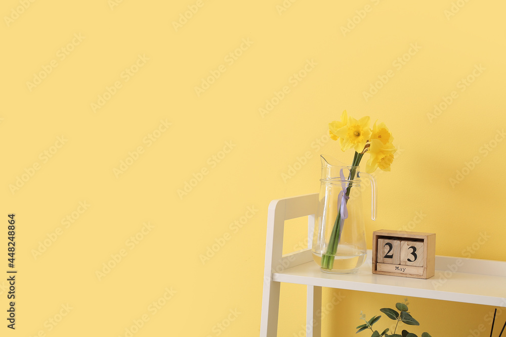 Jug with beautiful daffodils and calendar on table against color background
