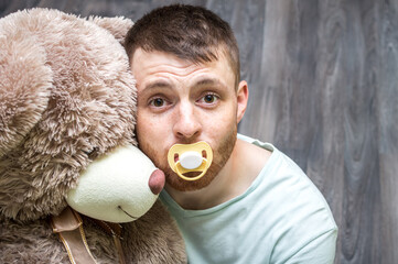 Portrait of a young man with a babys dummy in his mouth and play toy. Infantilism concept