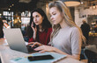© BullRun - Young women doing homework together on laptop from cafe