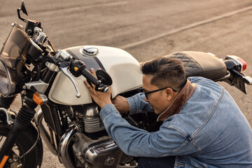 On the route to a summer vacation on a motorcycle, Biker guy On an asphalt highway, a crouching motorcyclist is concerned about a motorcycle breakdown.