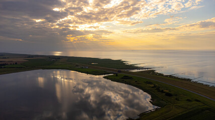 Der Deich zwischen der Nordsee und einem ruhigem Gewässer im Sonnenuntergang mit einigen Wolken