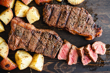 Grilled NY Strip Steak with Coffee Rub and Roasted Potatoes: Grilled New York strip steaks with roasted potatoes on a dark wood background